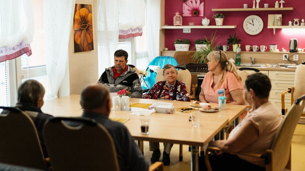 Seniors enjoying a meal in a nursing home dining room with caregivers in Karviná, Czechia.